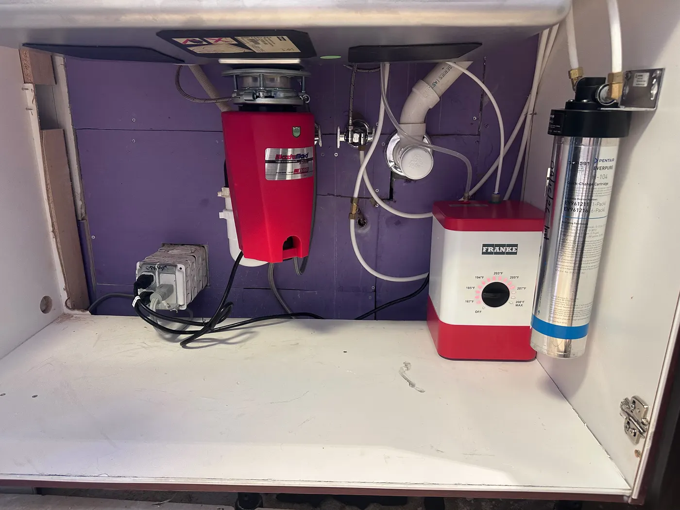 Under-sink cabinet with a new red garbage disposal, a water filtration system and tidy white drain lines