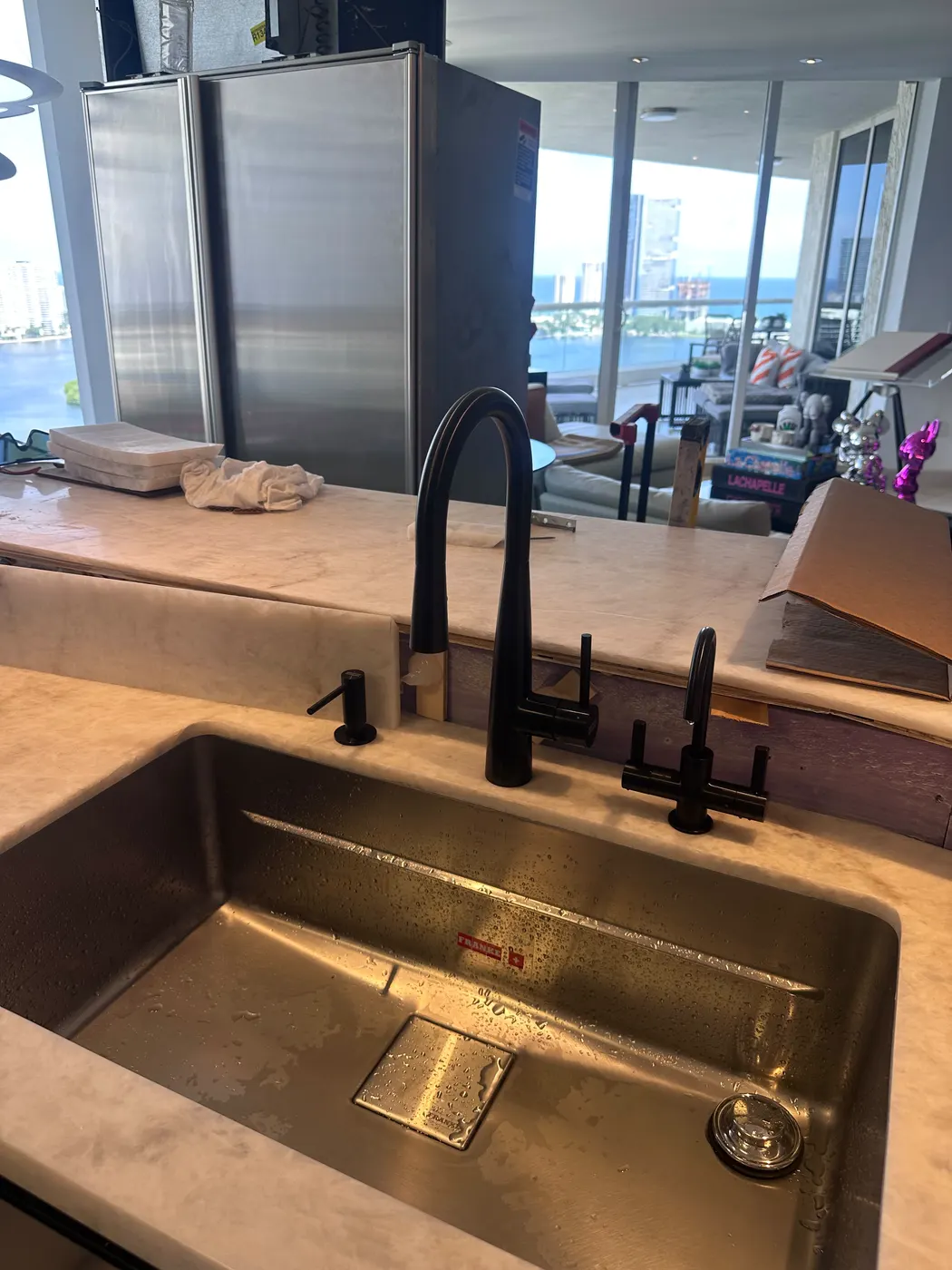 New undermount stainless kitchen sink with a matte black pull-down faucet and matching soap dispenser, city view through the windows