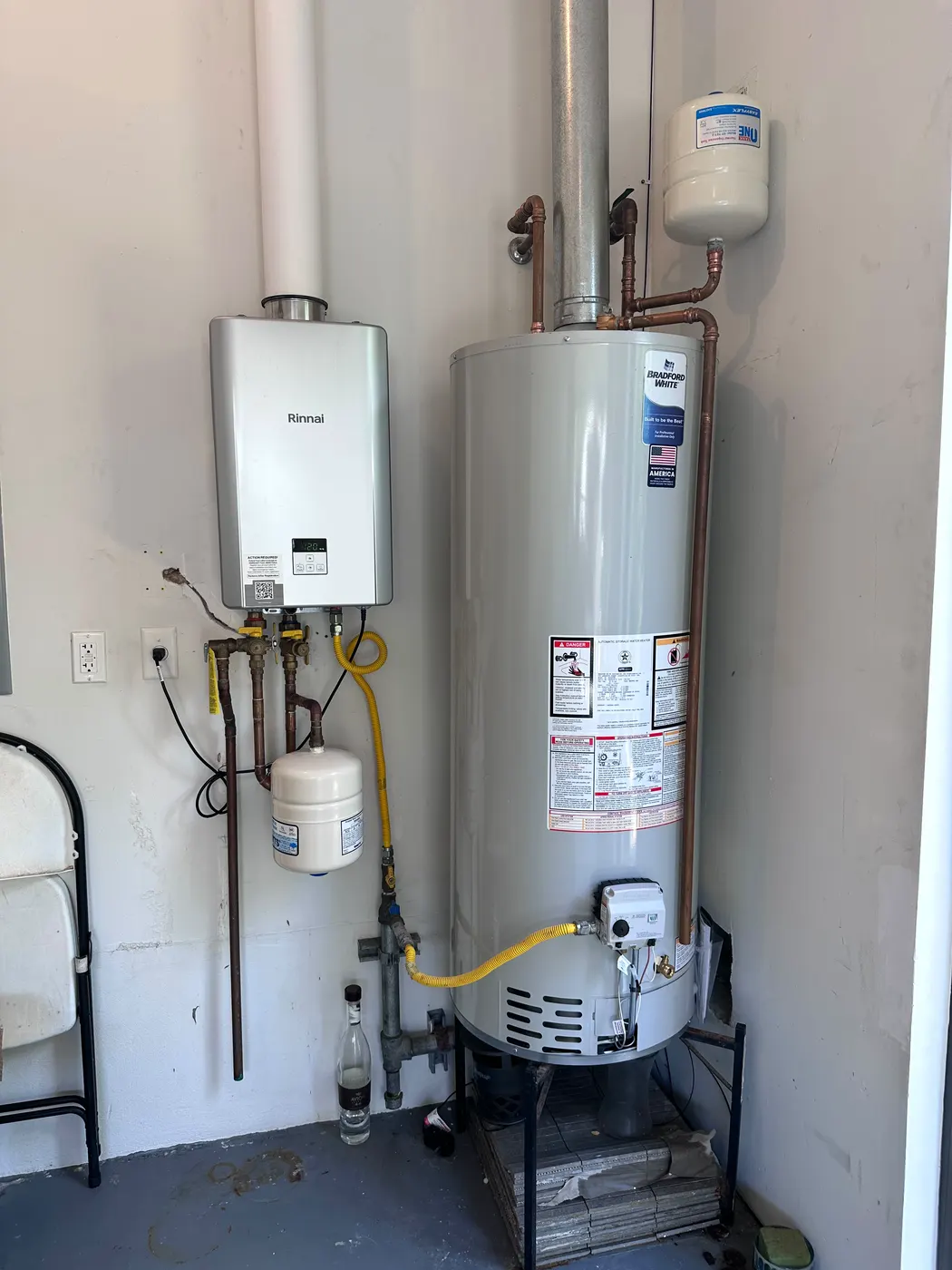 Finished garage installation: a new gas tank water heater next to a wall-mounted tankless unit, with new gas line, expansion tank and drain pan