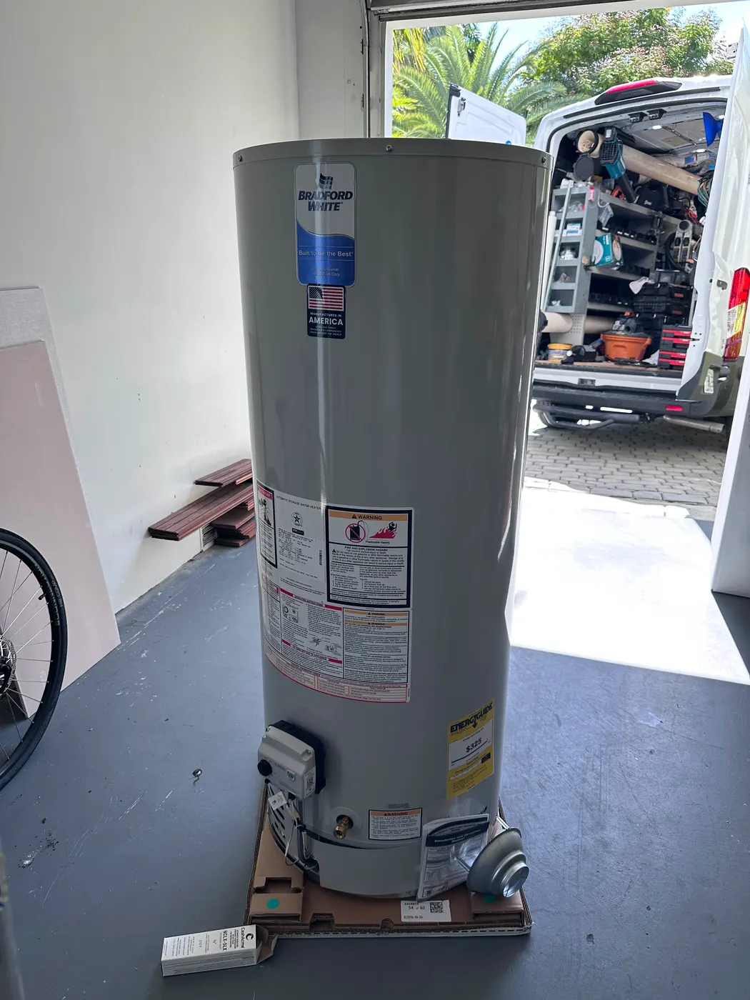 A new gas water heater standing in a garage with the open Full House work van behind it